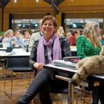 Landesvorsitzende Sigi Hagl bei Ihrer Verabschiedung: Sie sitzt auf ihrem Platz und schaut nach oben zur Bühne, wo ihr Ko-Vorsitzender Eike Hallitzky gerade die Laudatio auf sie hält.