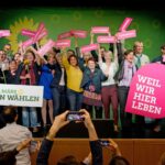 Zur Kommunalwahl 2020 in Bayern treten so viele grüne Kandidat*innen wir noch nie an. Einige davon haben sich auf dem Landesparteitag in Lindau zum Gruppenfoto auf der Bühne versammelt. Sie halten Schilder mit den Aufschriften "Weil wir hier leben" und "Am 15. März grün wählen"
