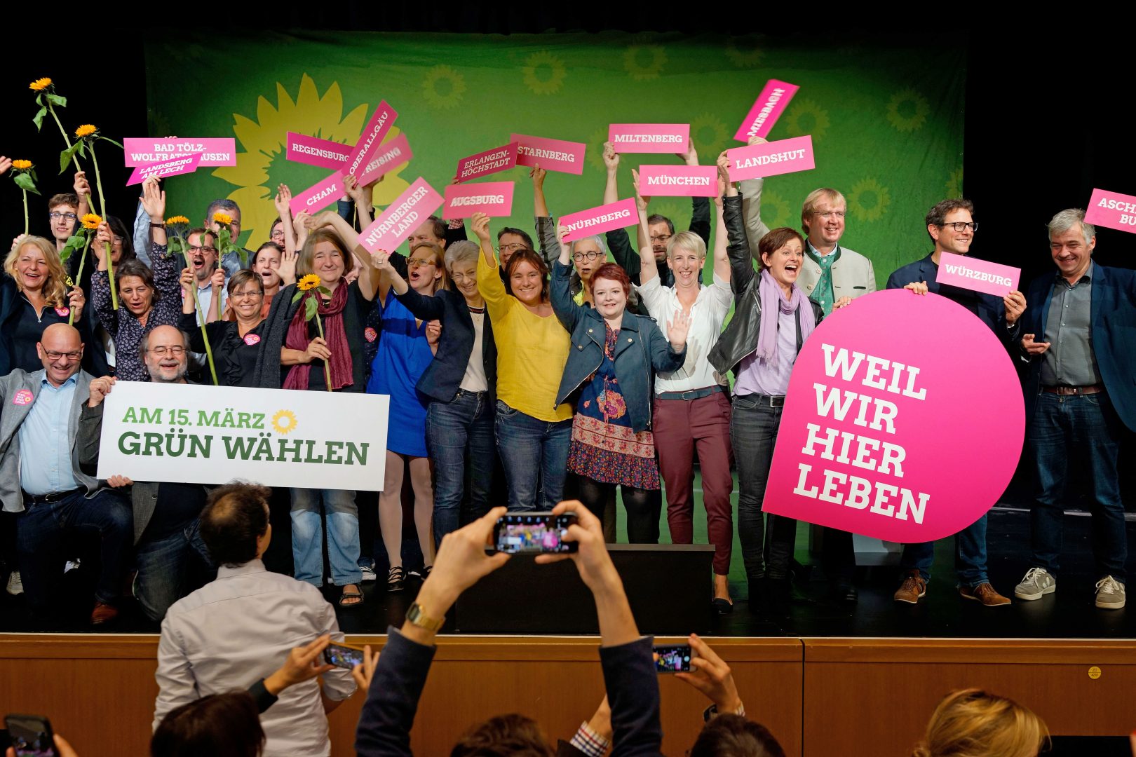 Zur Kommunalwahl 2020 in Bayern treten so viele grüne Kandidat*innen wir noch nie an. Einige davon haben sich auf dem Landesparteitag in Lindau zum Gruppenfoto auf der Bühne versammelt. Sie halten Schilder mit den Aufschriften "Weil wir hier leben" und "Am 15. März grün wählen"