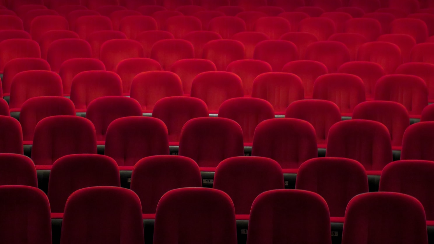 Blick in die leeren Stuhlreihen eines Kinos oder Theaters; die Stühle sind mit rotem Samt bezogen