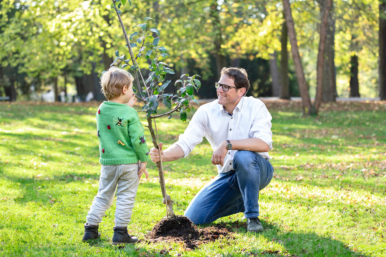 Martin Heilig und ein kleiner Junge sind auf einer Wiese und pflanzen zusammen einen Baum ein.