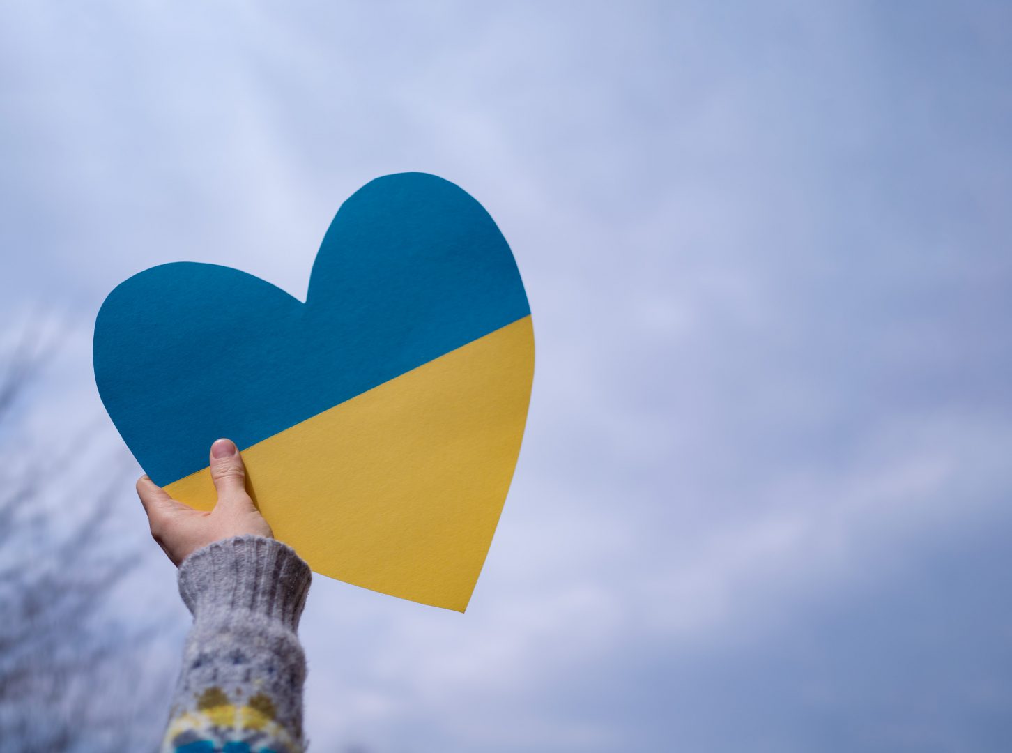 Nahaufnahme einer Hand, die ein Herz in den Landesfarben der Ukraine in den Himmel hält